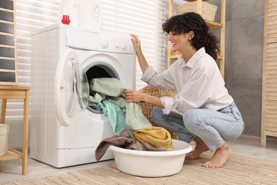 Photo of Woman taking laundry out of washing machine indoors