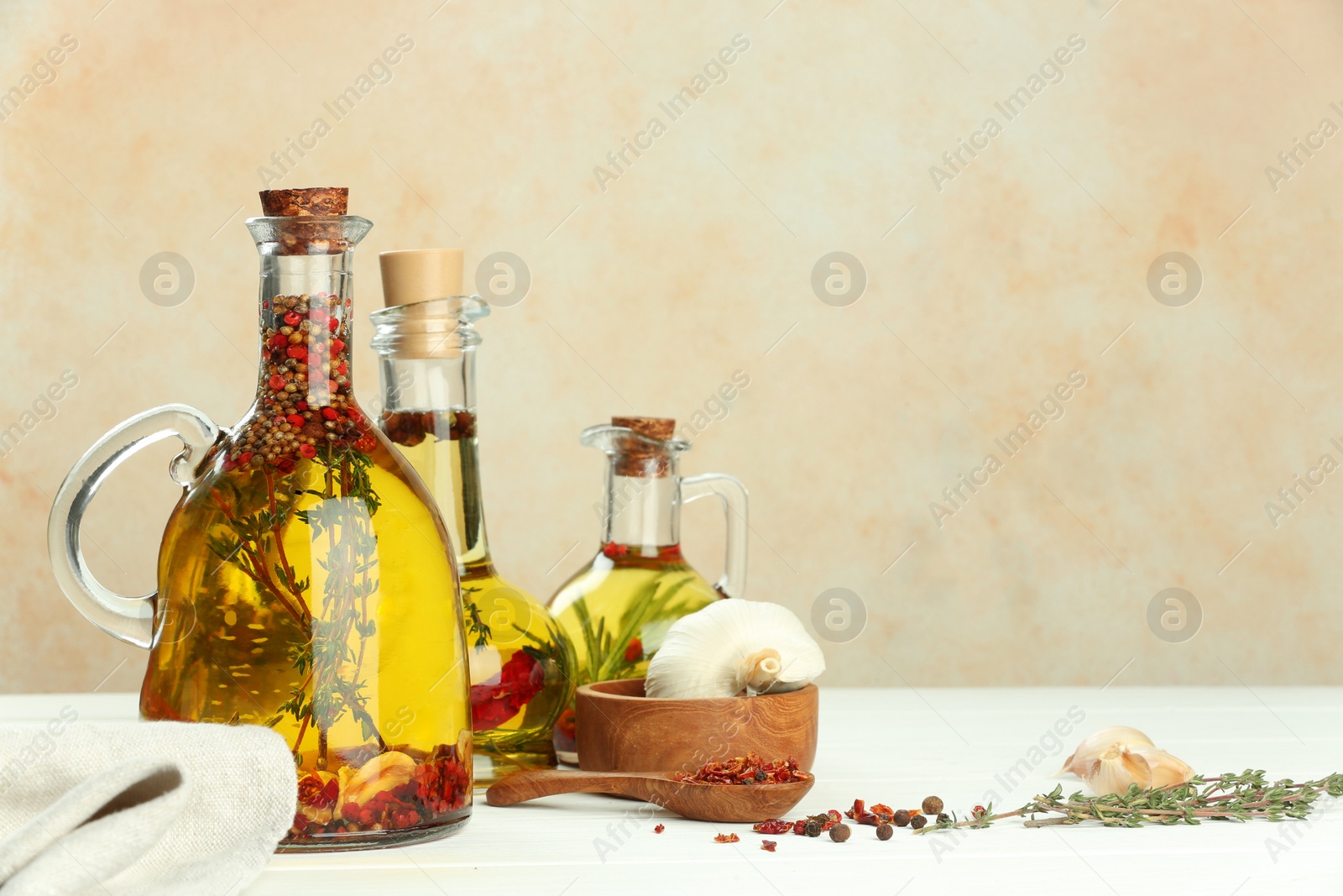 Photo of Cooking oil with different spices and herbs in jugs on white wooden table. Space for text