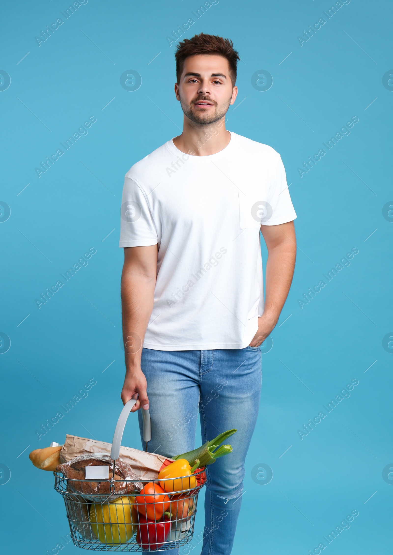 Photo of Young man with shopping basket full of products on blue background