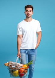 Young man with shopping basket full of products on blue background