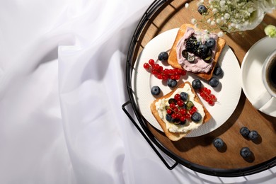 Photo of Tray with cup of coffee, cream cheese sandwiches and flowers on white fabric, top view. Space for text