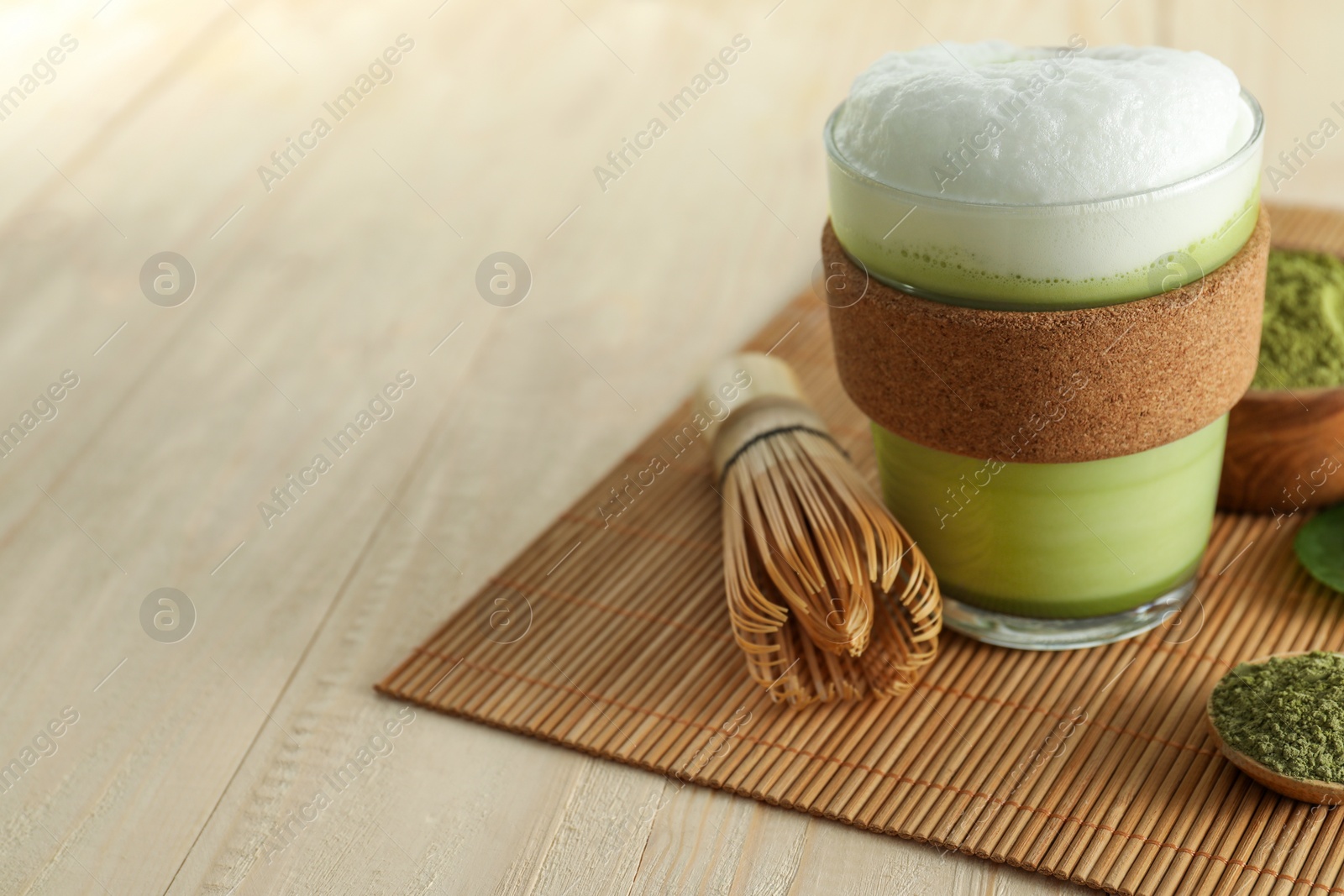 Photo of Glass cup of fresh matcha latte, powder and bamboo whisk on wooden table. Space for text