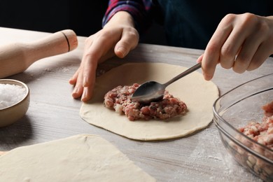 Woman making chebureki with meat at wooden table, closeup