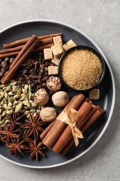 Plate with different aromatic spices on light textured table, top view