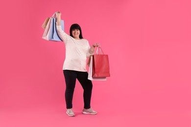 Photo of Beautiful overweight mature woman with shopping bags on pink background. Space for text