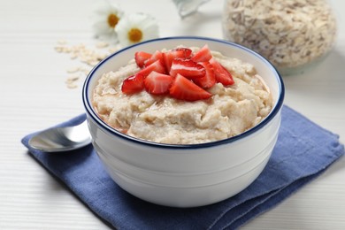 Photo of Tasty oatmeal porridge with strawberries served on white wooden table