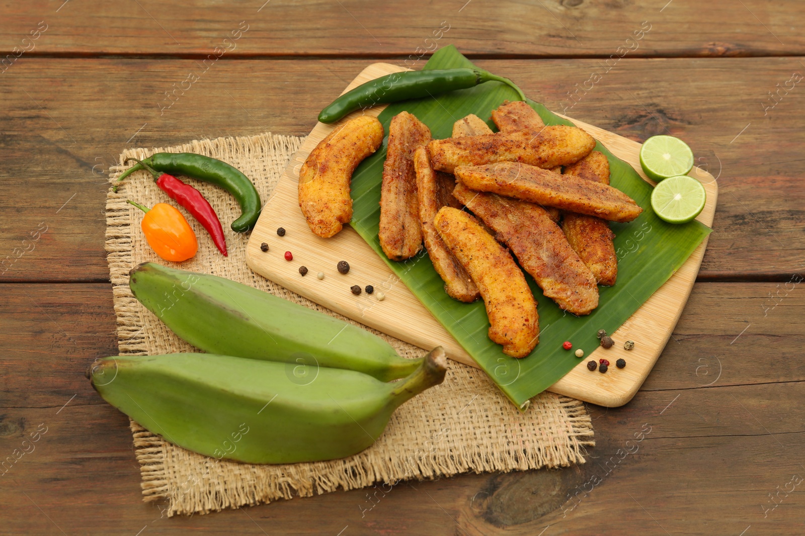 Photo of Delicious fried bananas, fresh fruits and different peppers on wooden table