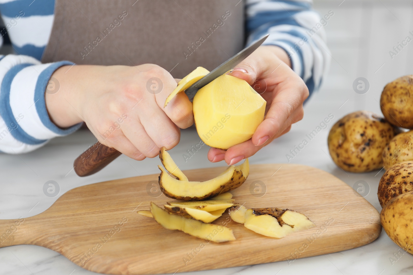 Photo of Woman peeling fresh potato with knife at white marble table, closeup