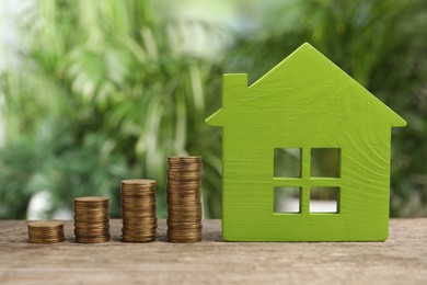 Photo of Mortgage concept. Model house and stacks of coins on wooden table against blurred green background, closeup