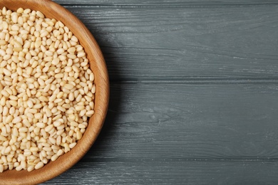 Dish with pine nuts on wooden background, top view. Space for text