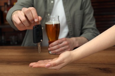 Man with glass of alcoholic drink giving car key to woman at table, closeup. Don't drink and drive concept