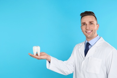 Photo of Male dentist holding tooth model on color background