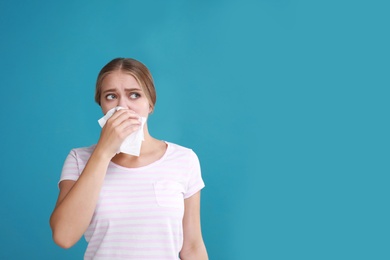 Photo of Young woman suffering from allergy on blue background. Space for text