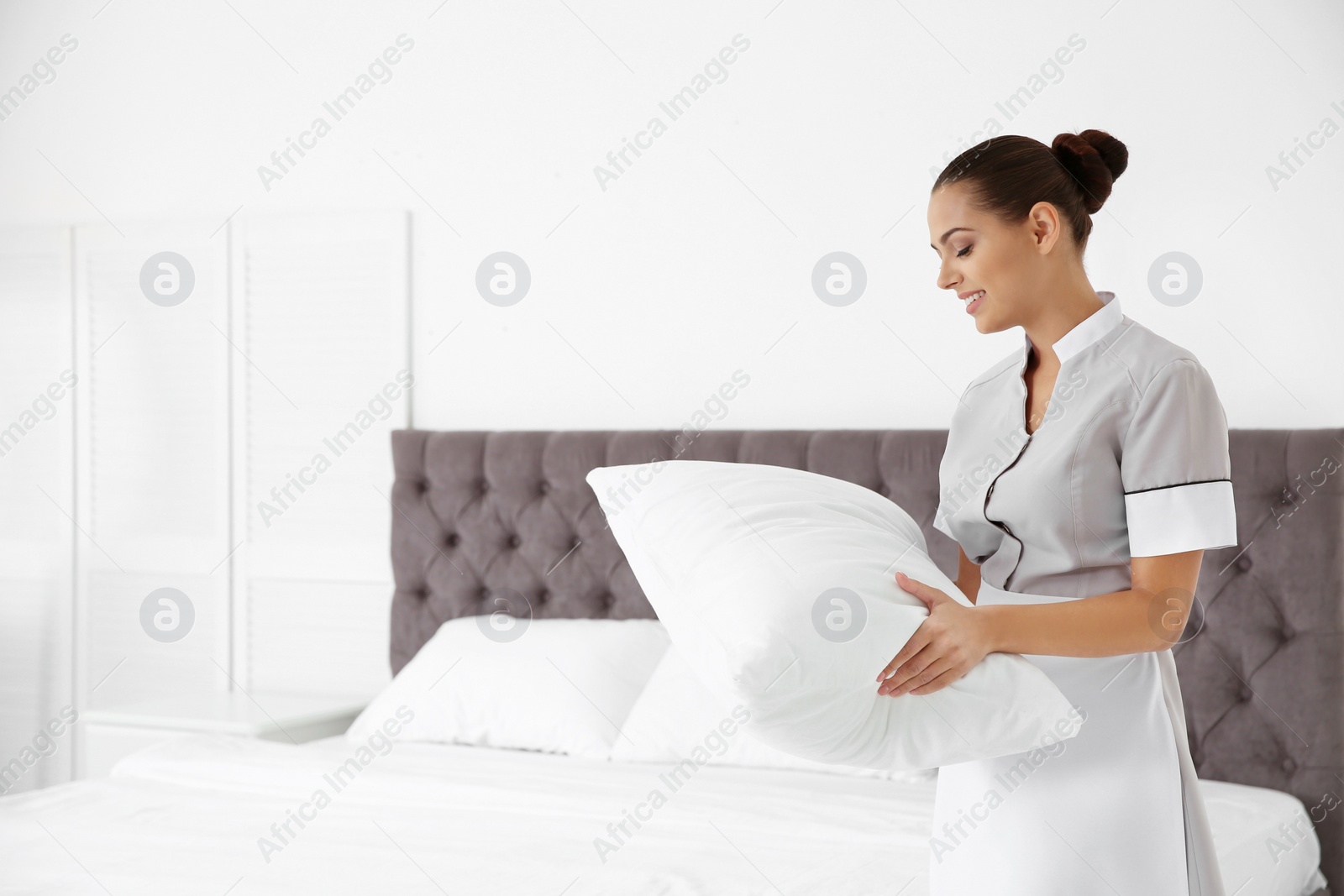 Photo of Young chambermaid with pillow in hotel room. Space for text