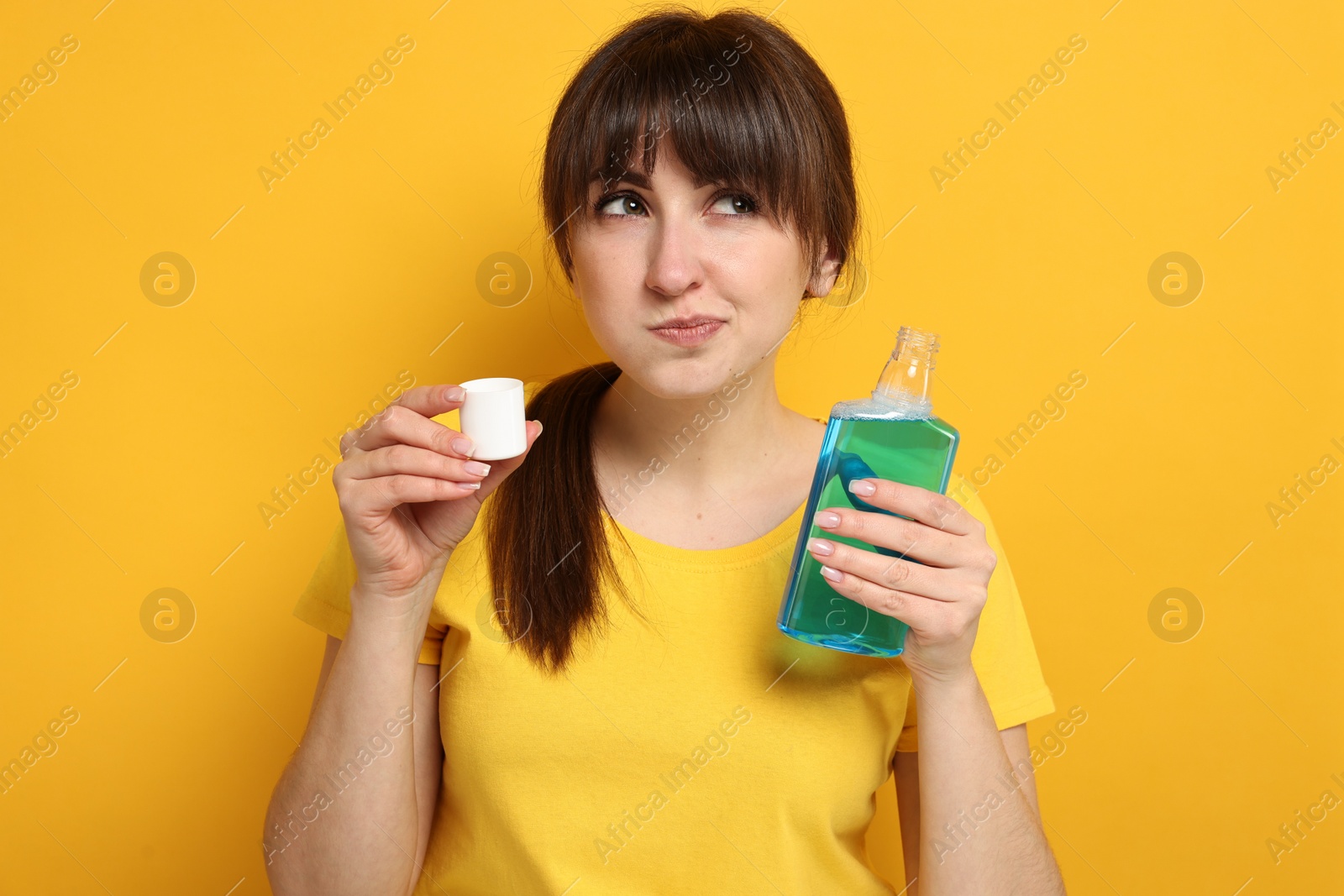 Photo of Young woman using mouthwash on yellow background