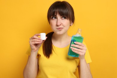 Young woman using mouthwash on yellow background