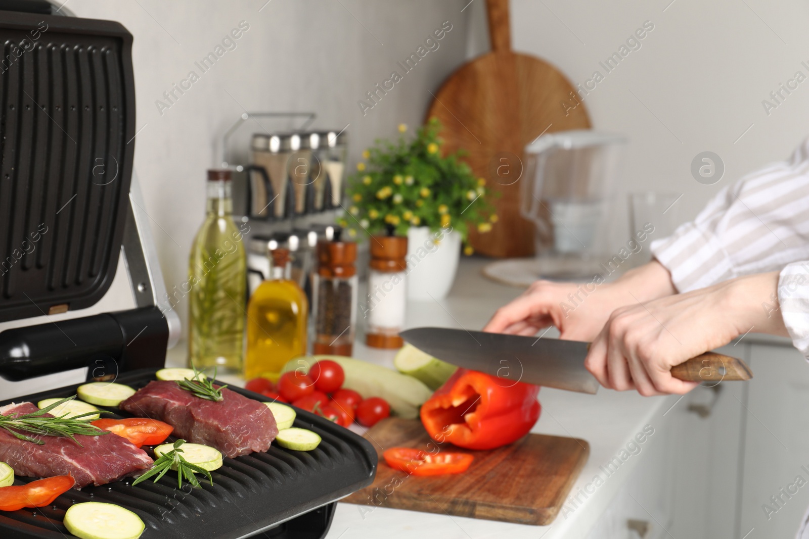 Photo of Woman cooking different products with electric grill at white wooden table in kitchen, closeup