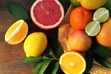 Photo of Different citrus fruits and leaves on wooden table, flat lay