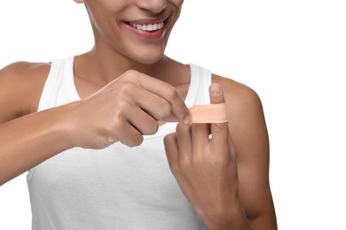 Man putting sticking plaster onto finger on white background, closeup