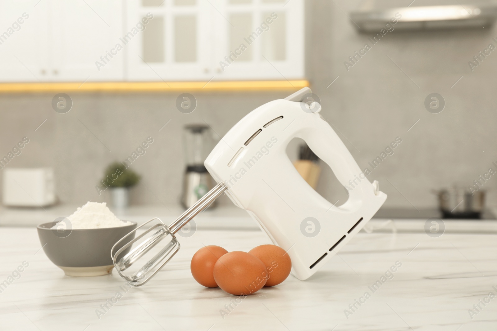 Photo of Modern mixer, eggs and bowl with flour on white marble table in kitchen