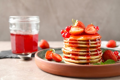 Delicious pancakes with fresh berries and syrup on beige marble table