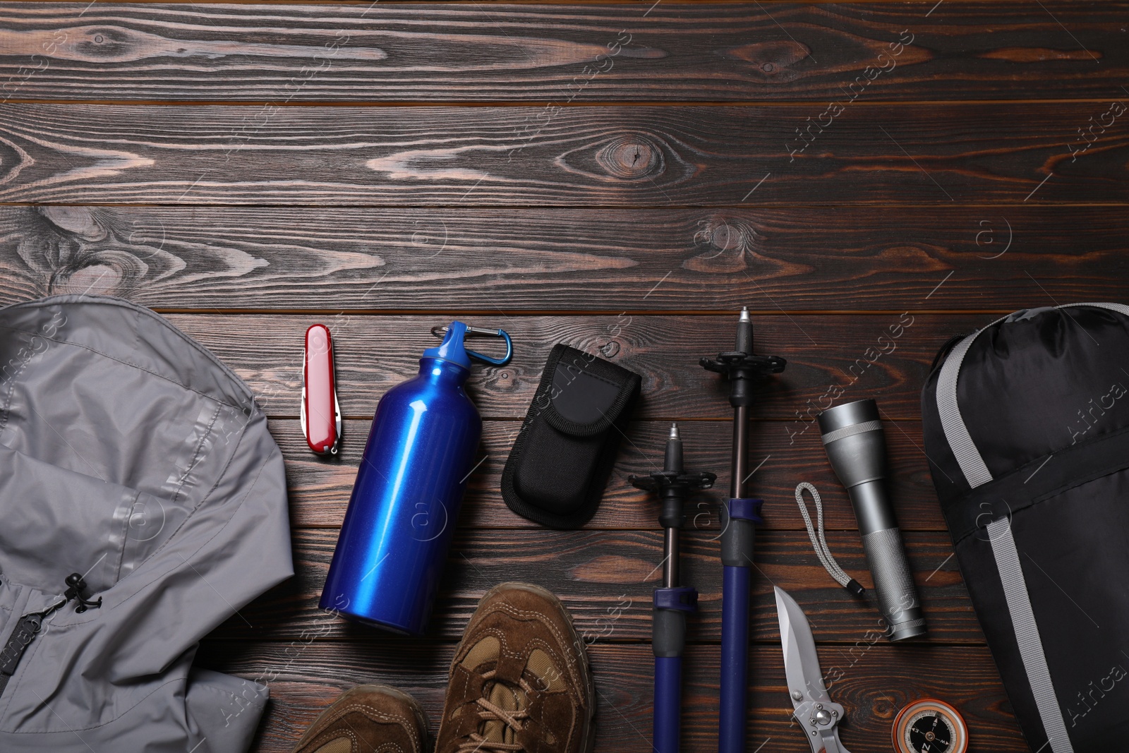 Photo of Flat lay composition with trekking poles and other hiking equipment on wooden background, space for text