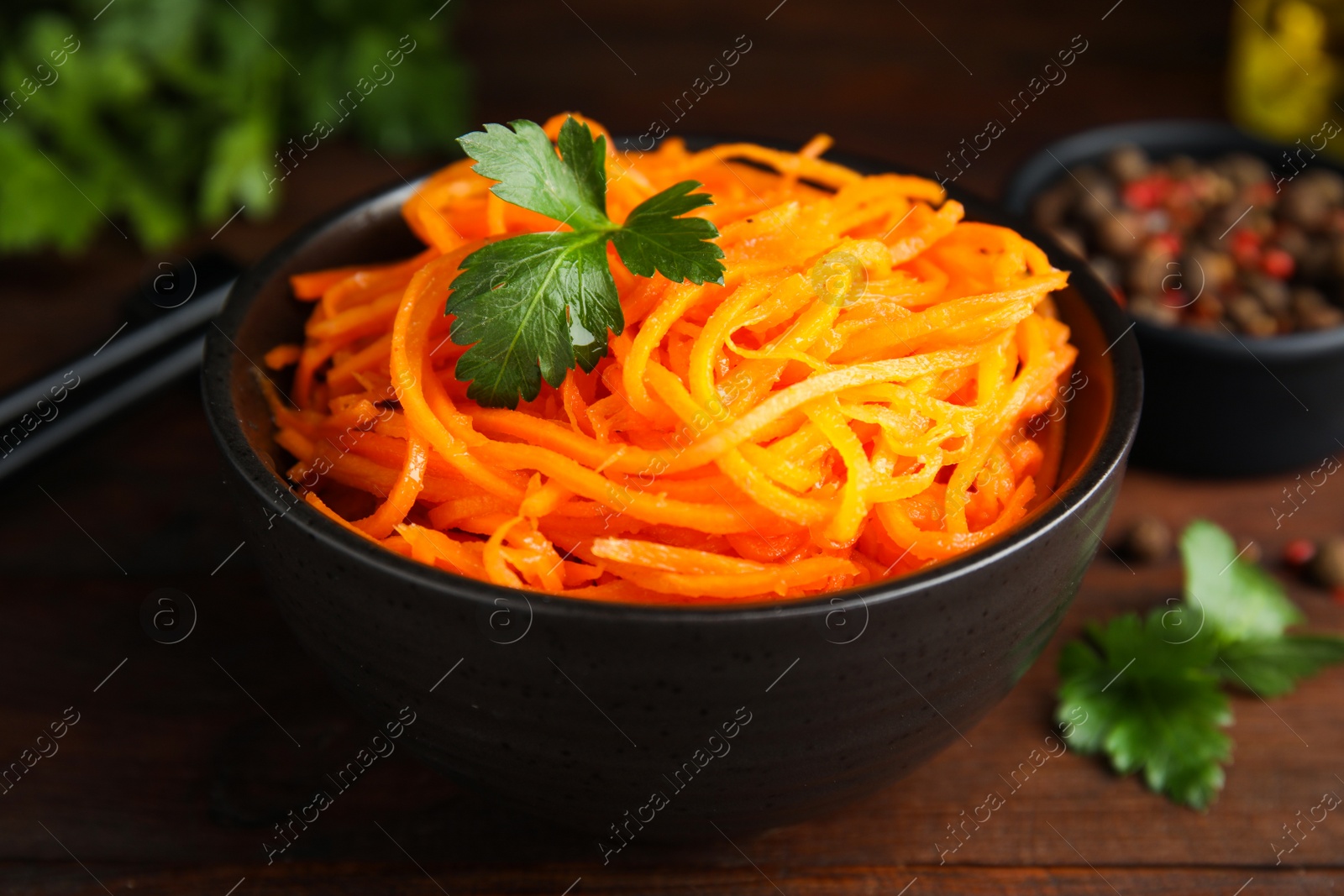 Photo of Delicious Korean carrot salad with parsley in bowl on wooden table, closeup