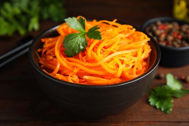Photo of Delicious Korean carrot salad with parsley in bowl on wooden table, closeup