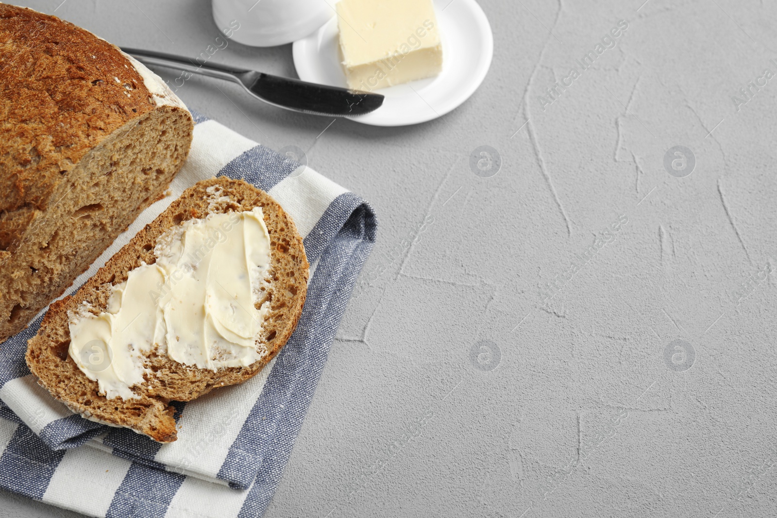 Photo of Slice of tasty bread with butter near loaf on grey table. Space for text