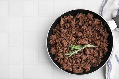 Photo of Fried ground meat in frying pan and rosemary on white tiled table, top view. Space for text