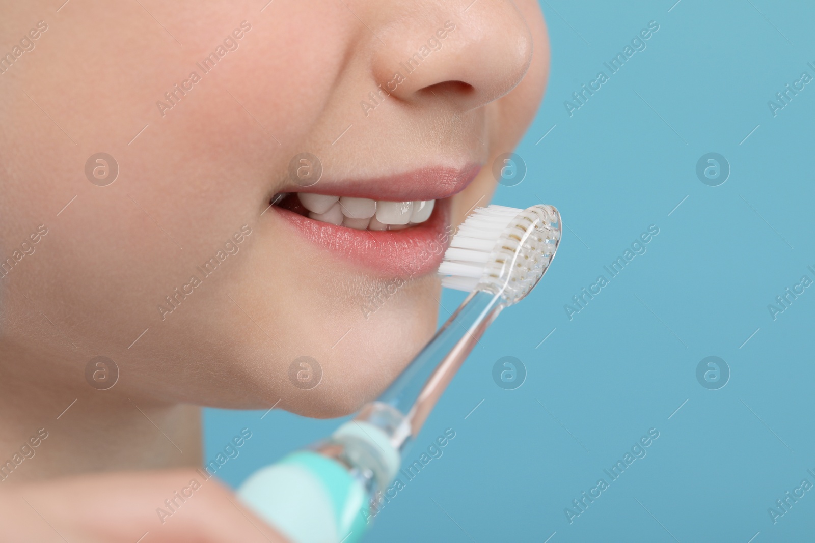 Photo of Girl brushing her teeth with electric toothbrush on light blue background, closeup. Space for text