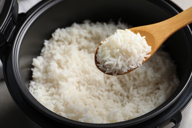 Spoon with tasty hot rice over cooker, closeup