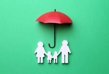 Photo of Mini umbrella and family figure on green background, flat lay