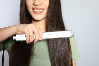 Happy woman using hair iron on grey background, closeup