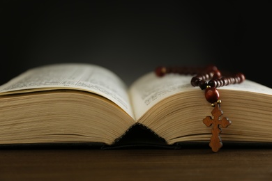 Open Bible and rosary beads on wooden table, closeup. Lent season