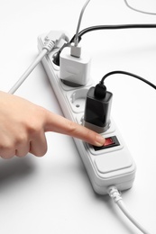 Woman pressing power button of extension cord on white background, closeup. Electrician's professional equipment