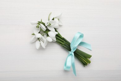 Photo of Beautiful snowdrop flowers with ribbon on white wooden table, top view