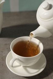 Pouring aromatic tea in cup at gray table, closeup