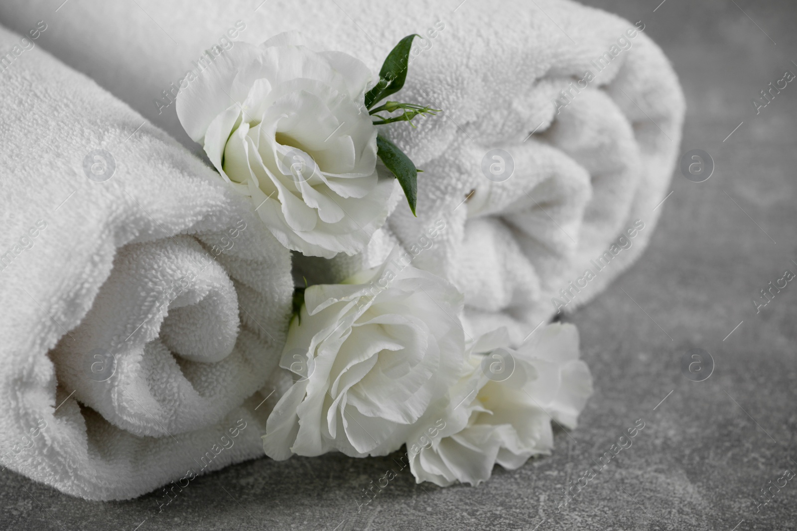 Photo of White soft towels with flowers on grey table, closeup