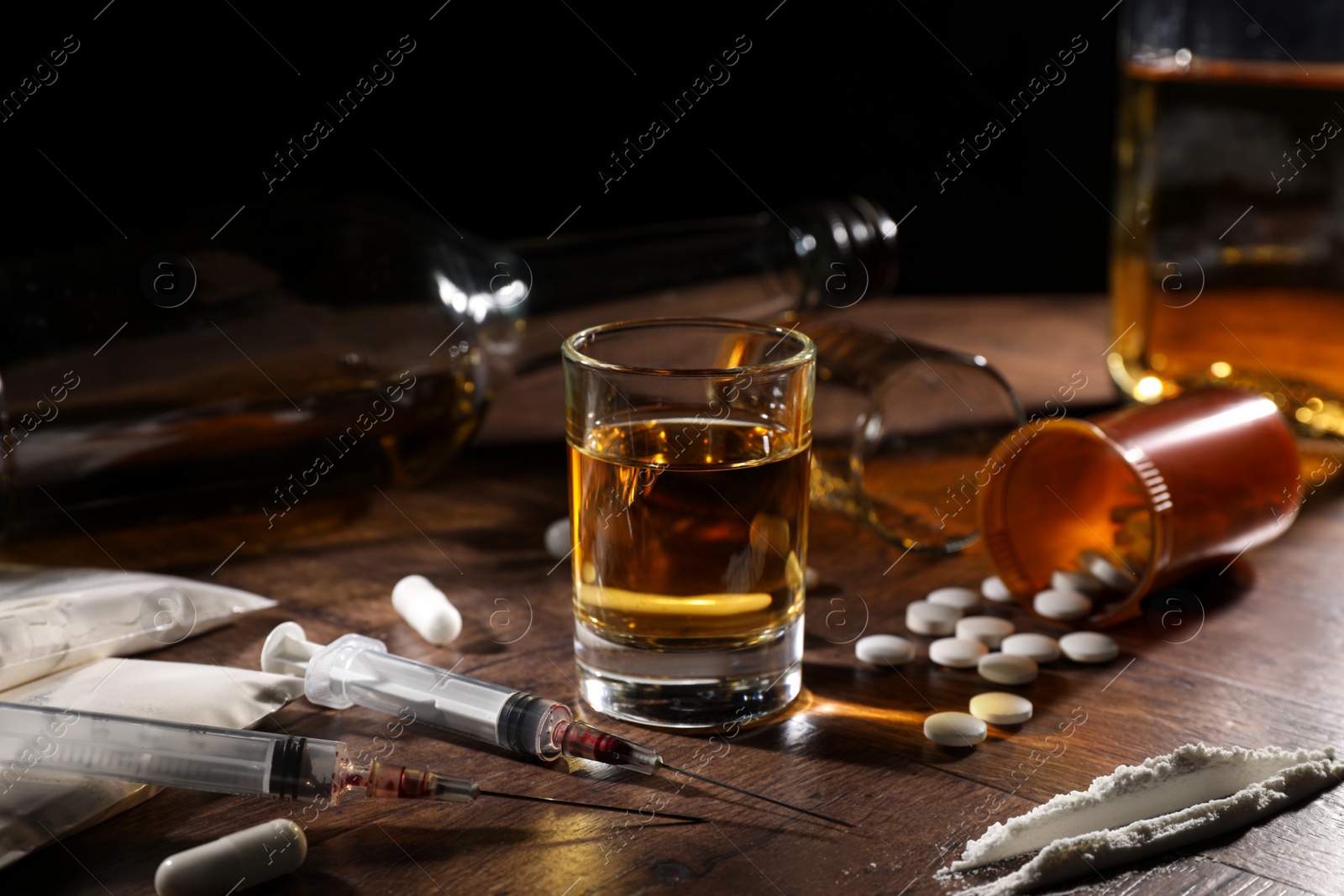 Photo of Alcohol and drug addiction. Whiskey in glass, syringes, pills and cocaine on wooden table