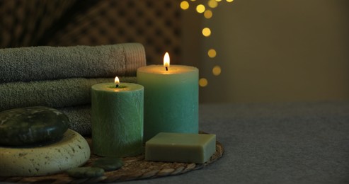 Photo of Spa composition. Burning candles, stones, soap and towels on grey table, space for text