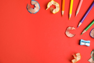 Color pencils, sharpener and shavings on red background, flat lay. Space for text