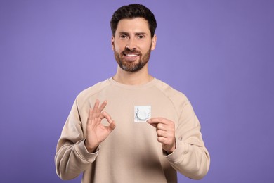 Photo of Man with condom showing ok gesture on purple background. Safe sex