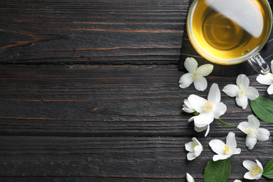 Flat lay composition with cup of tea and fresh jasmine flowers on black wooden table. Space for text