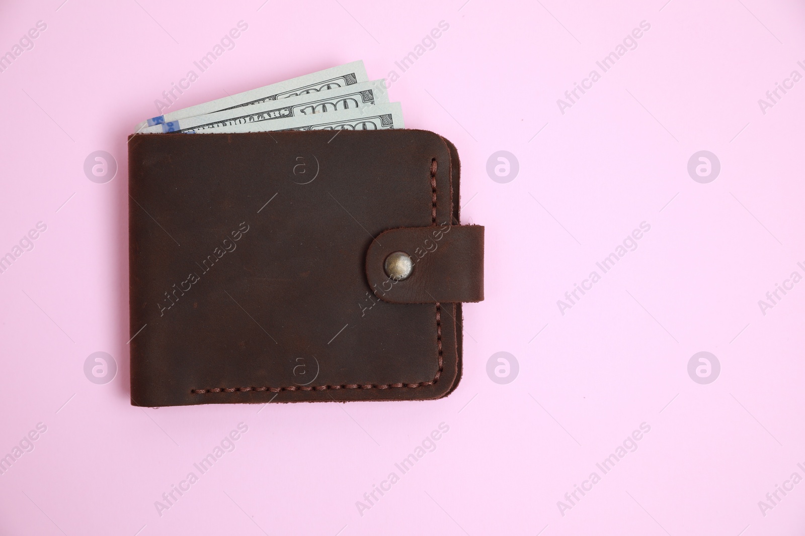 Photo of Stylish brown leather wallet with dollar banknotes on pink background, top view. Space for text