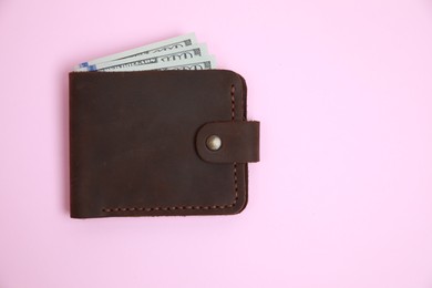Photo of Stylish brown leather wallet with dollar banknotes on pink background, top view. Space for text