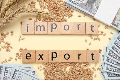 Photo of Words Import and Export made of wooden squares, ears of wheat and banknotes on beige background, flat lay