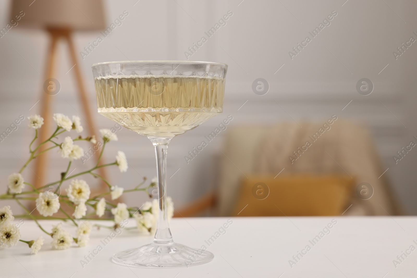 Photo of Glass of alcohol drink and flowers on table in room, space for text. Relax at home