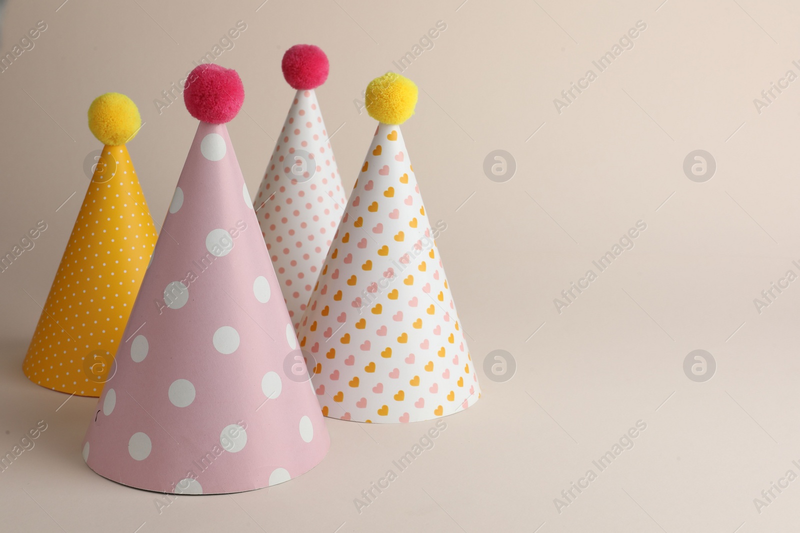 Photo of Beautiful party hats with pompoms on beige background. Space for text