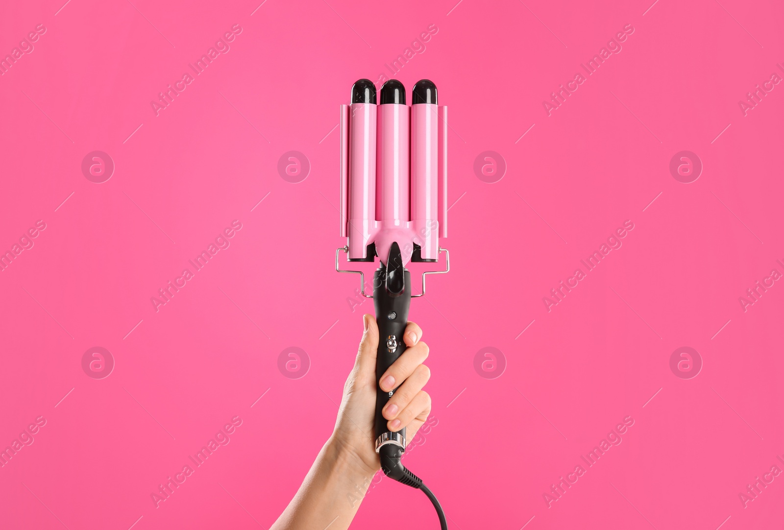 Photo of Woman holding triple curling hair iron on pink background, closeup